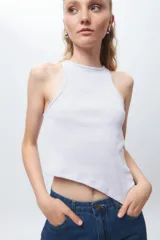 Top de algodón blanco sin mangas con cuello halter y bajo asimétrico en punta diagonal. Presenta un tejido de punto acanalado y un diseño inspirado en la estética de los años 2000.