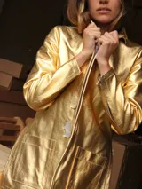 Blazer de cuero metalizado en color dorado, con cuello clásico, cierre frontal con botones de nácar y bolsillos frontales tipo parche.