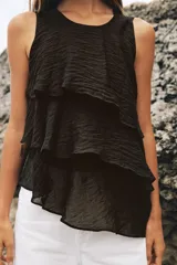 Top de cuello redondo y manga sisa, confeccionado en tejido con acabado satinado. Presenta volantes en cascada y un diseño de bajo asimétrico, con cierre en la espalda mediante pequeña abertura y botón.