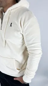 Canguro color crema de tela peluche con capucha, cierre de cremallera corto y bolsillo tipo canguro. Logo de la marca bordado en negro en el pecho.