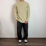 Sweater de tejido de punto grueso color verde militar, con cuello redondo y mangas largas tipo raglán. Presenta un corte holgado y una pequeña etiqueta con logo en el puño.