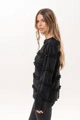 Blusa negra plisada de manga larga con detalles de volados horizontales en el frente y las mangas.