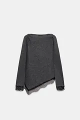 Top de manga larga en tejido suave color gris, con cuello redondo y bajo asimétrico decorado con encaje negro a tono. Presenta detalles de encaje negro en los puños.