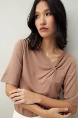 Remera de modal color marrón topo, manga corta, con escote asimétrico y detalle de nudo con frunces en el centro del pecho.
