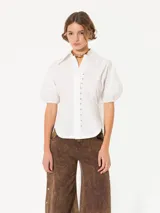 Camisa blanca de popelina, con cuello clásico, mangas cortas abullonadas y cierre frontal con ganchos metálicos.
