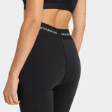 Calza deportiva New Balance Rise Sport Legging 25, color negro, de tiro alto con cintura elástica que lleva el logo de la marca repetido.