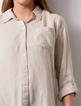 Camisa blanca de lino con cuello con solapa, manga larga regulable con presilla y botón, y abertura central con botones.