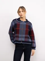 Campera de punto con diseño a cuadros tartán en tonos marrones y beige. Presenta un corte oversize, cierre frontal con cremallera, cuello tipo babero con volados y mangas largas con puños ajustados.