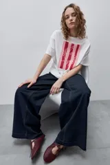 Remera blanca de calce relajado y silueta amplia, con cuello redondo, mangas cortas y estampa gráfica frontal de un cangrejo sobre franjas en tonos rosado y rojo.