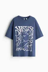 Remera oversized de algodón color azul, con hombros caídos, cuello redondo y estampa gráfica frontal de estilo artístico en tono claro.