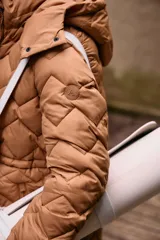 Campera larga color marrón con diseño acolchado, capucha desmontable, cierre frontal con botones a presión, bolsillos laterales con cierre, puños elásticos y cintura ajustable.