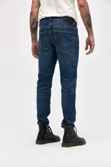 Jean de corte slim, entallado en cadera y muslos con ajuste gradual desde la rodilla hasta el tobillo. Presenta un lavado azul oscuro clásico con costuras reforzadas y cierre frontal con botón y cremallera.
