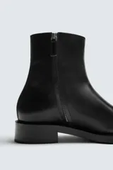 Bota de cuero negro con diseño minimalista, punta fina, cierre lateral con cremallera y tacón bajo.