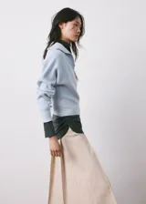 Sweater de punto celeste con cuello polo y cierre frontal en V, manga larga con puños ajustados y diseño acanalado.