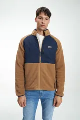 Buzo sherpa color camel con paneles acolchados azul marino en el pecho y los hombros. Tiene cuello alto, cierre frontal completo y bolsillos laterales con cierre.