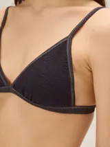 Conjunto de bikini negro de textura acanalada con sutiles destellos brillantes, compuesto por un corpiño triangular con detalle de volado lateral y una bombacha clásica tipo vedetina.