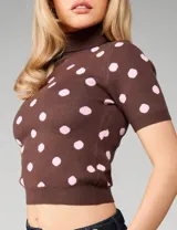 Sweater de punto color chocolate con estampado de lunares rosados, cuello alto y mangas cortas. Presenta un calce ajustado al cuerpo con terminaciones acanaladas en cuello, mangas y ruedo.