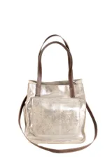 Cartera tipo bolso de cuero con acabado metalizado plateado, cuenta con doble asa corta y una correa larga ajustable. Presenta un bolsillo frontal externo y cierre superior.