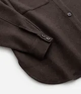 Camisa de corte largo tipo shacket, confeccionada en polivelour color marrón. Presenta cuello camisero, cierre frontal con botones, hombros caídos, mangas largas y dos bolsillos frontales aplicados con solapa.