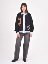 Cardigan de punto negro con diseño de sol en color tostado, cuello redondo y cierre frontal con botones. Presenta un tejido con motas de colores y corte holgado.