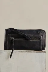 Billetera de cuero color negro con acabado gastado, diseño alargado, cierre perimetral de cremallera y tirador de cuero trenzado. Cuenta con bolsillo exterior con cierre y marca grabada en el frente.