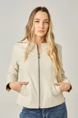 Campera clásica de cuero ovino color beige claro, con cuello a la base, cierre frontal y bolsillos laterales con cierre. Presenta costuras verticales que estilizan la silueta.