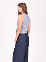 Chaleco sin mangas de color beige con rayas verticales blancas. Presenta un diseño cruzado tipo wrap con escote en V y ajuste mediante lazo lateral.