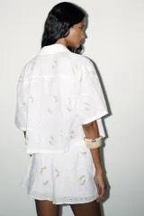 Shorts blancos con cintura elástica, bolsillos laterales ocultos y forro interior. Presenta bordados de flores en tonos rosados y amarillos.