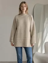 Sweater de punto color crema, con cuello alto y diseño holgado. Presenta puños y ruedo acanalados con detalle de líneas horizontales en la parte inferior.