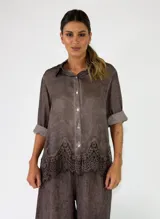 Camisa de manga larga color marrón con efecto desteñido, cuello camisero, cierre frontal de botones y detalle de encaje aplicado en el ruedo inferior.