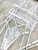 Conjunto de lencería de cuatro piezas en color blanco, confeccionado en encaje con diseño floral. Incluye bralette triangular, tanga de tiro alto con tiras ajustables, portaligas integrado y ligas para las piernas.