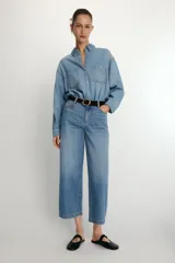 Camisa de denim de corte oversize con cuello solapa, manga larga con puños, cierre frontal con botones a presión y bolsillos de plastrón en el delantero.