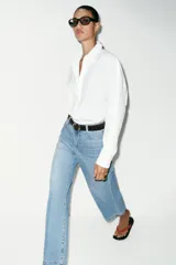 Jeans de tiro alto con pernera ancha y corte cropped. Presenta diseño de cinco bolsillos, cierre frontal con cremallera y botón, e incluye un cinturón oscuro con hebilla metálica.