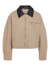Chaqueta estilo worker de gabardina en color beige, con cuello camisero de cuerina negra, cierre frontal de cremallera y bolsillos frontales con cierre y ribete.