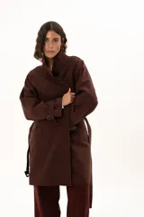 Trench color chocolate con cuello alto, cierre frontal con botones y cinturón ajustable en la cintura. Presenta mangas largas con puños ajustables mediante tiras y hebillas, y bolsillos frontales.