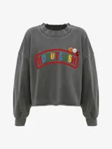 Buzo de algodón gris oscuro con efecto lavado, cuello redondo y mangas largas con puños acanalados. Presenta un estampado frontal con el texto "HOT & FLASH" en colores vivos y tres pines decorativos. El ruedo inferior es cortado y deshilachado.