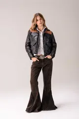 Chaqueta de cuero de estilo western, con diseño bicolor en negro y detalles en cuero marrón en la parte superior. Presenta bolsillos frontales con solapa, cierre de botones a presión y tachas metálicas decorativas.