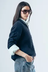 Sweater de punto grueso color azul marino, con cuello polo y cierre frontal parcial. Presenta un diseño de tejido trenzado en el centro y mangas largas con puños acanalados.