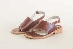 Sandalias de cuero color marrón, con tira ancha sobre los dedos, tira trasera con hebilla y suela plana.