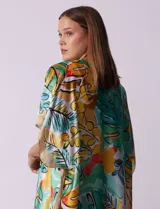 Kimono de satén con estampado tropical y hojas en tonos verdes, amarillos y naranjas sobre fondo claro. Tiene mangas anchas y corte abierto.