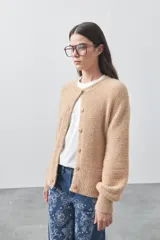 Cardigan de textura suave y efecto fluffy, color beige, con cuello redondo, cierre frontal con botones y puños acanalados.