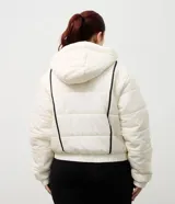 Campera puffer deportiva Get Over, color blanco con detalles de bies en color negro a lo largo de las mangas. Presenta cuello alto con capucha integrada, cierre frontal con botones a presión, bolsillos laterales con cremallera y puños con elásticos.