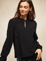Blusa negra de manga larga con cuello mao y pequeña abertura frontal con cierre de botón. Presenta un diseño fluido con frunces en el escote y puños elásticos.