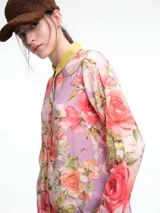 Camisa de silueta relajada con estampado floral en tonos rosas y violetas. Presenta cuello camisero en color amarillo mostaza, cierre frontal con botones, y puños con detalle de estampado animal print. El ruedo tiene un acabado festoneado.
