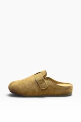 Zueco de gamuza color marrón camel, con diseño cerrado en la parte delantera y tira ajustable con hebilla metálica en el empeine.