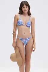 Top de bikini triangular con estampado floral en tonos rosados y verdes sobre fondo azul cielo. Tirantes finos con detalle trenzado.