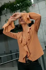 Blusa color beige con escote en V, volados frontales y mangas largas acampanadas.