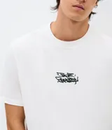 Remera de algodón con cuello redondo y manga corta. Presenta un diseño con estampa pequeña en el pecho y un gráfico estilo graffiti en la espalda.
