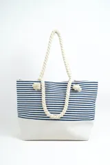 Bolso tipo tote de playa, con diseño de rayas horizontales en color gris y base blanca. Cuenta con asas de soga gruesa en color crudo con nudos decorativos.