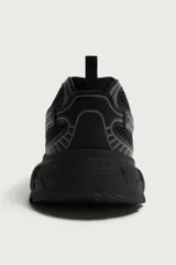 Zapatilla deportiva tipo running de color negro, confeccionada en una combinación de piezas de malla y material sintético. Presenta un diseño con cordonera curvada y una suela de volumen con diseño irregular.